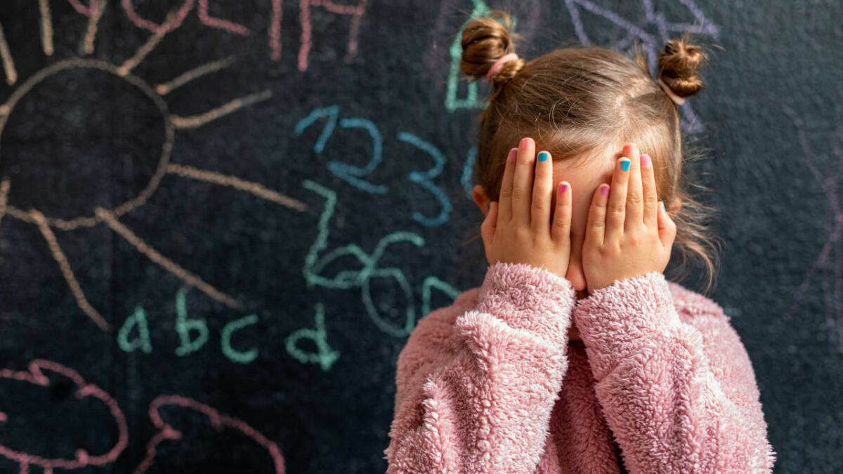 bambina che si copre gli occhi davati ad una lavagna nera con disegni a gessetti colorati