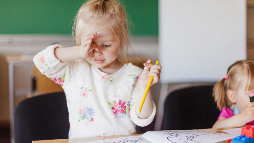 bambina stanca che si sfrega gli occhi e tiene in mano una matita