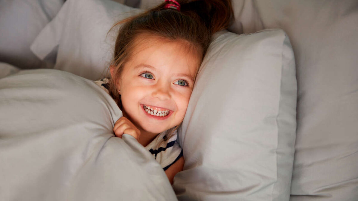 bambina sorridende distesa a letto sotto le le coperte e testa su di un cucino