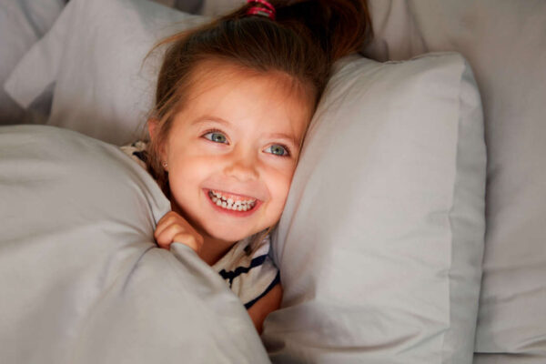 bambina sorridende distesa a letto sotto le le coperte e testa su di un cucino