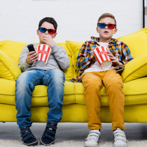 due bambini che guardano la tv su un divano giallo mangiando popcorn