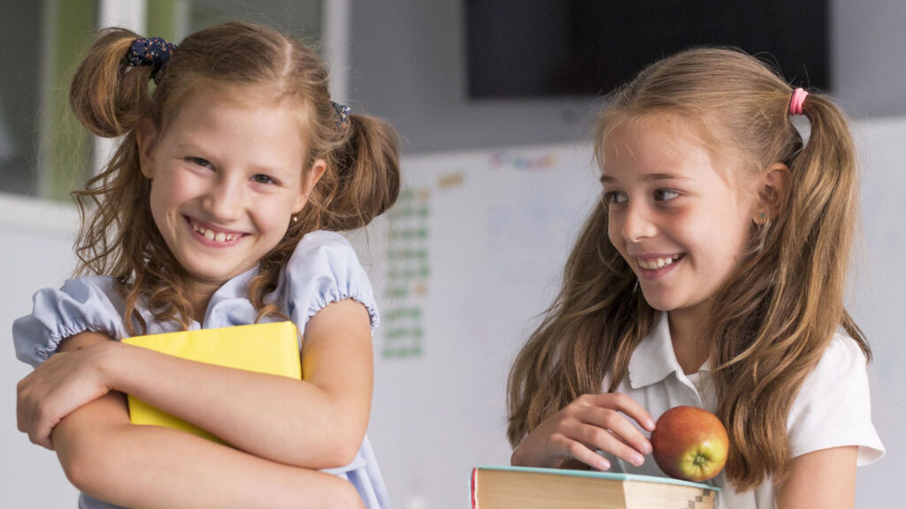 due bambine sorridenti con i libri di scuola ed una mela in mano