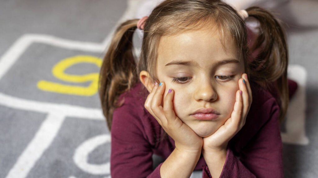 bambina distesa prona che si tiene il mento con espressione malinconica